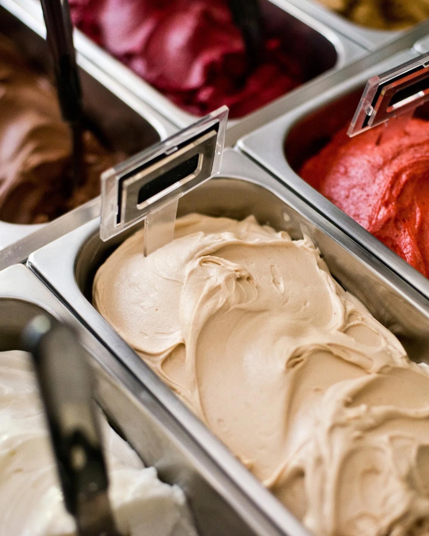 Assorted ice cream flavors in stainless steel tubs, with creamy beige gelato in the foreground.