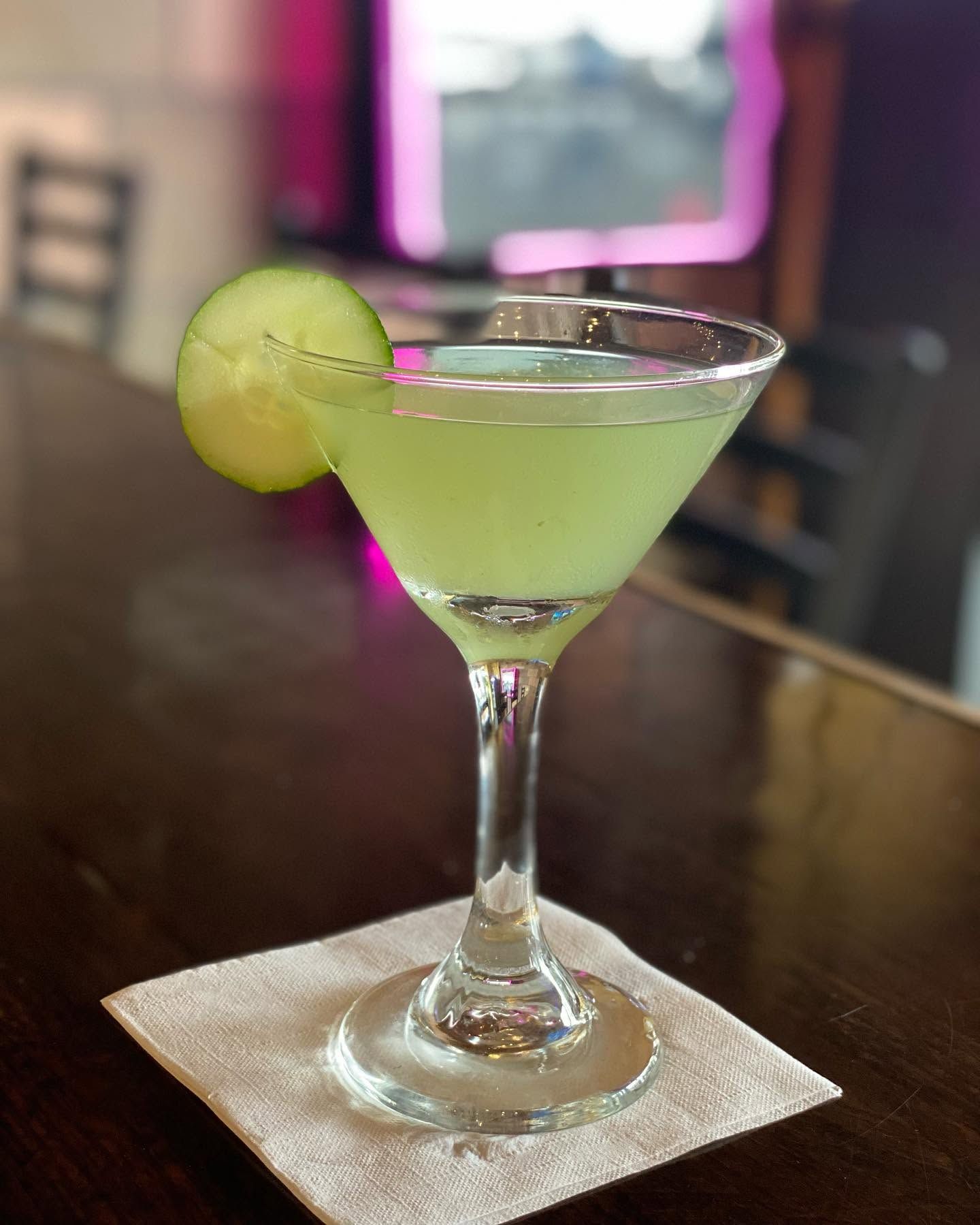 Green martini with lime garnish on a napkin on a bar table, with a blurred lounge background