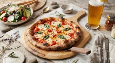 Wooden table with margherita pizza, salad, bread, and a glass of beer in a cozy meal setting