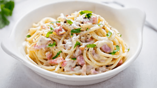 Creamy spaghetti carbonara in a white bowl, topped with bacon bits and parsley