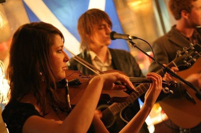 Musicians playing violin and guitars on stage under warm orange lighting