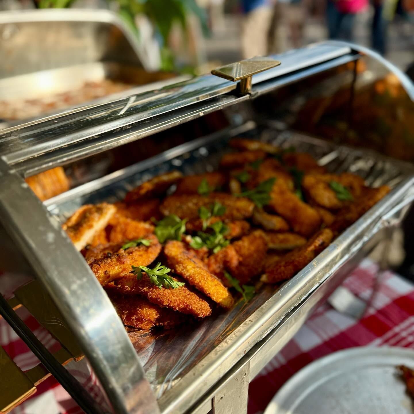 Open buffet tray of fried chicken wings with herbs on a checkered tablecloth