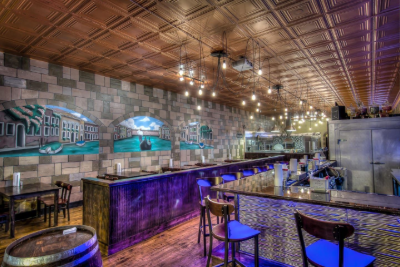 Stylish bar interior with wood ceiling, purple-lit counter, and empty tables under hanging lights