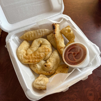 Takeout container with fried pastries and a cup of dipping sauce on a wooden table