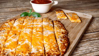 Cheesy pizza slices on a wooden board with marinara dipping sauce and basil