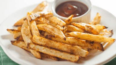 Seasoned French fries on a white plate with a small cup of dipping sauce
