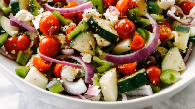 Colorful chopped vegetable salad with cherry tomatoes, cucumber, red onion, and feta in a white bowl