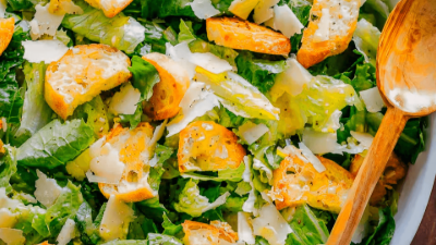 Fresh salad with romaine, orange slices, and shaved cheese, tossed in creamy dressing with a wooden spoon