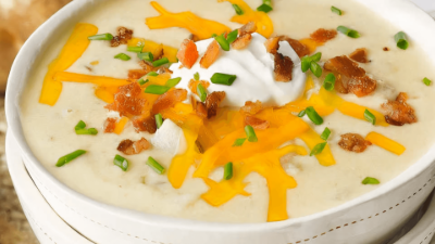 Bowl of creamy potato soup topped with shredded cheddar, bacon bits, sour cream, and chives
