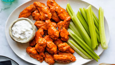 Buffalo chicken wings with ranch dip and celery sticks on a white plate