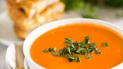 Bowl of creamy orange soup topped with herbs, served on a white table