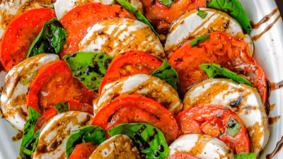 Sliced caprese salad with tomatoes, mozzarella, basil, and balsamic drizzle on a white plate