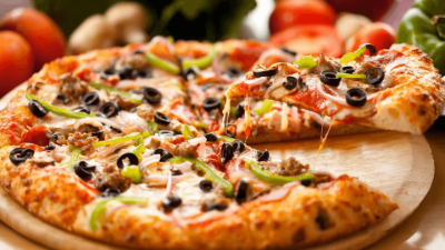 Two cheese pizzas topped with olives, peppers, and basil on a wooden board