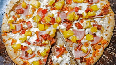 Pizza with pineapple, ham, and melted cheese on a wooden board, with a slice cut out
