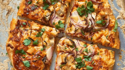 Sliced pizza topped with browned cheese, onions, and cilantro on parchment paper