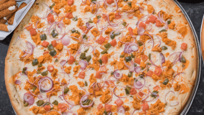Overhead view of a pizza topped with shrimp, tomatoes, onions, and herbs on a baking tray