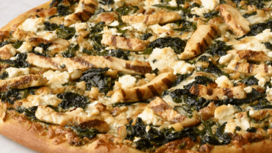 Close-up of a cheesy spinach pizza with crisscrossed crust on a baking tray