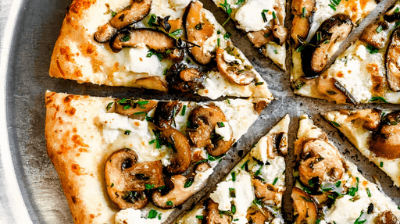 Sliced mushroom pizza on a white plate, topped with herbs and cheese