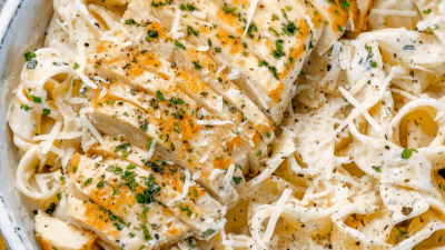 Creamy pasta topped with sliced chicken, grated cheese, and parsley
