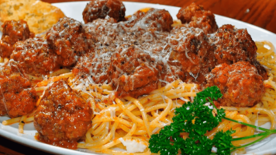 Spaghetti topped with meatballs and tomato sauce, garnished with parsley on a white plate