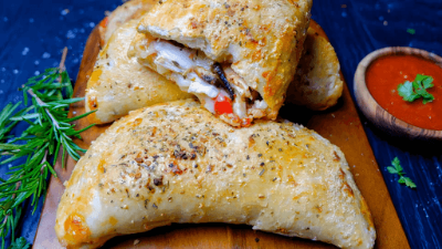Golden baked calzone on a board with herbs and red dipping sauce