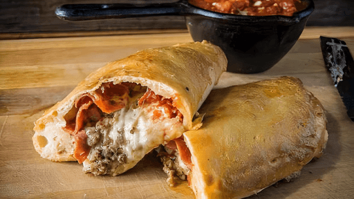 Sliced stromboli with melted cheese and pepperoni on a wooden board, with a bowl of marinara sauce behind it