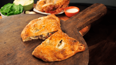 Golden fried pastries on a wooden board with a small dipping sauce cup and greens in the background