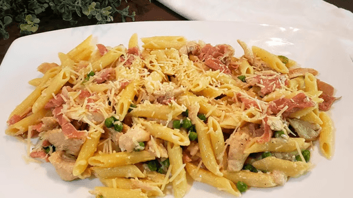 Penne pasta with creamy sauce, shredded cheese, and bits of ham on a white plate