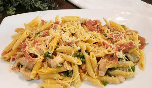 Plate of penne pasta with creamy sauce, tomatoes, herbs, and grated cheese