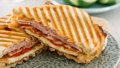 Grilled ham and cheese panini cut in half on a plate, with golden toasted bread and melted filling