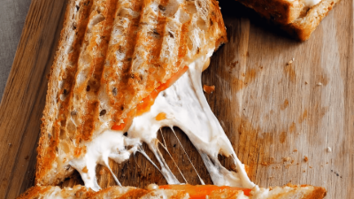 Grilled panini sandwich with melted cheese stretching on a wooden board