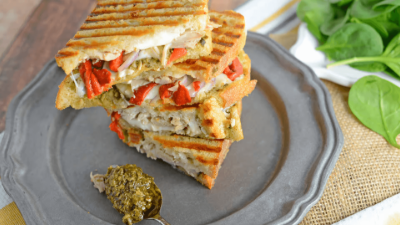 Grilled sandwich wedges with melted filling on a plate, served with green pesto and basil.