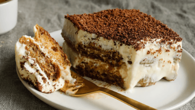 Slice of tiramisu dessert on a white plate with a gold fork