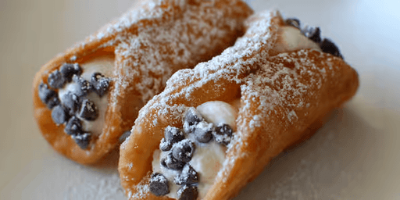 Two powdered cannoli with chocolate chip filling on a light surface