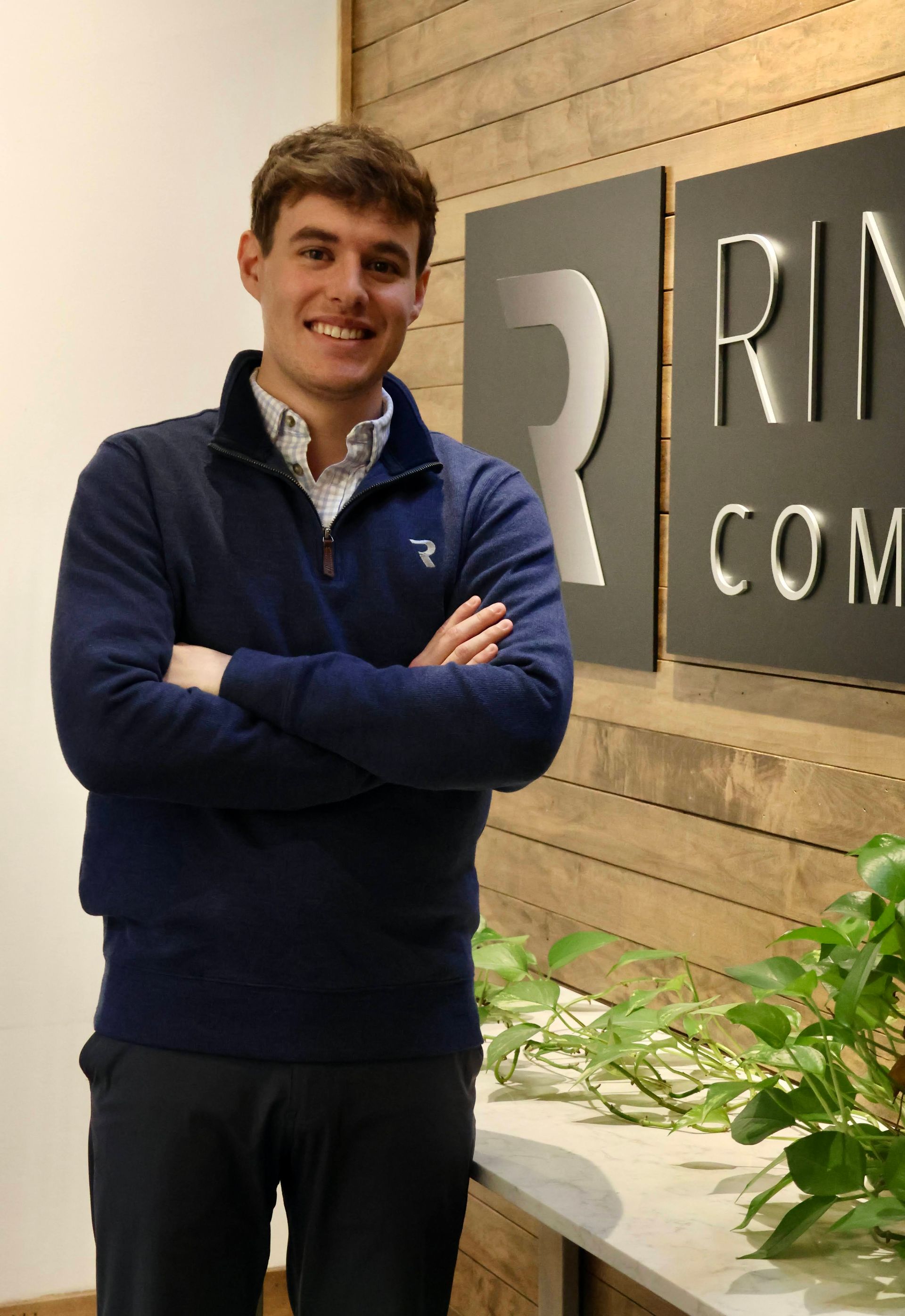 Smiling person in a light gray pullover seated indoors by a window and desk