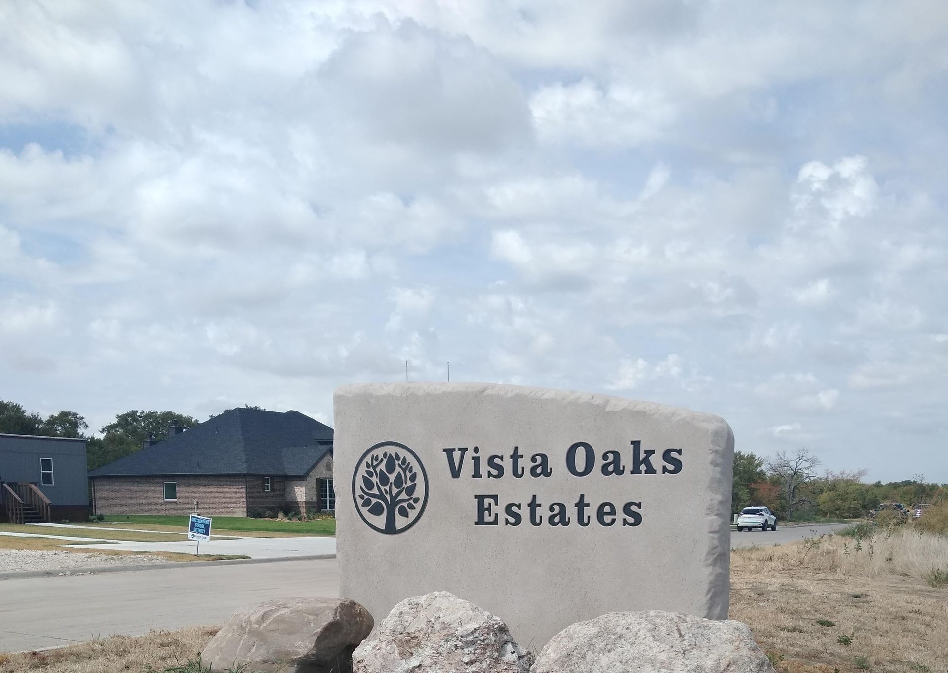 A sign for vista oaks estates is sitting on a rock