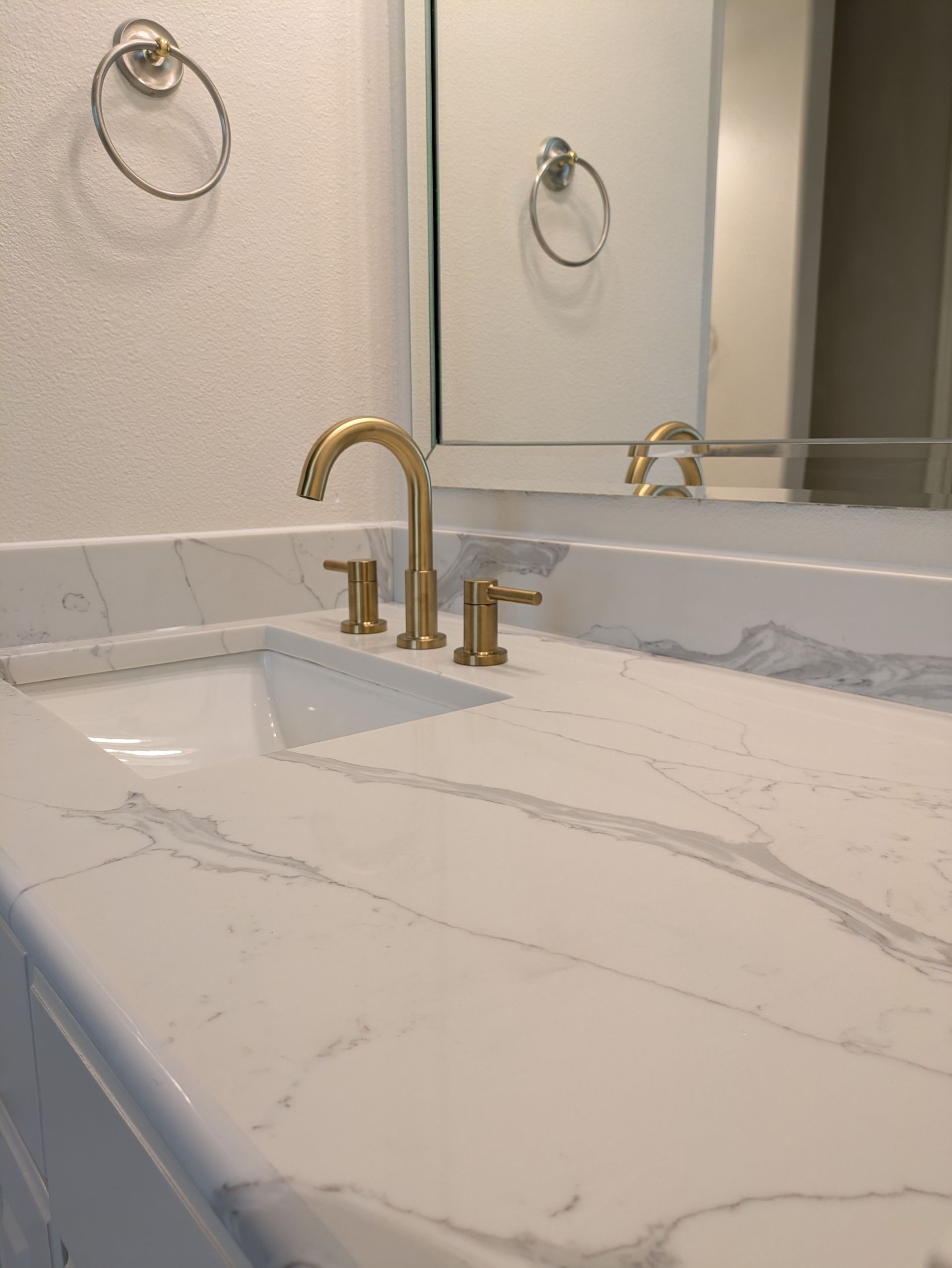 Gold faucet and fixtures on a white marble countertop with a built-in sink and a mirror.
