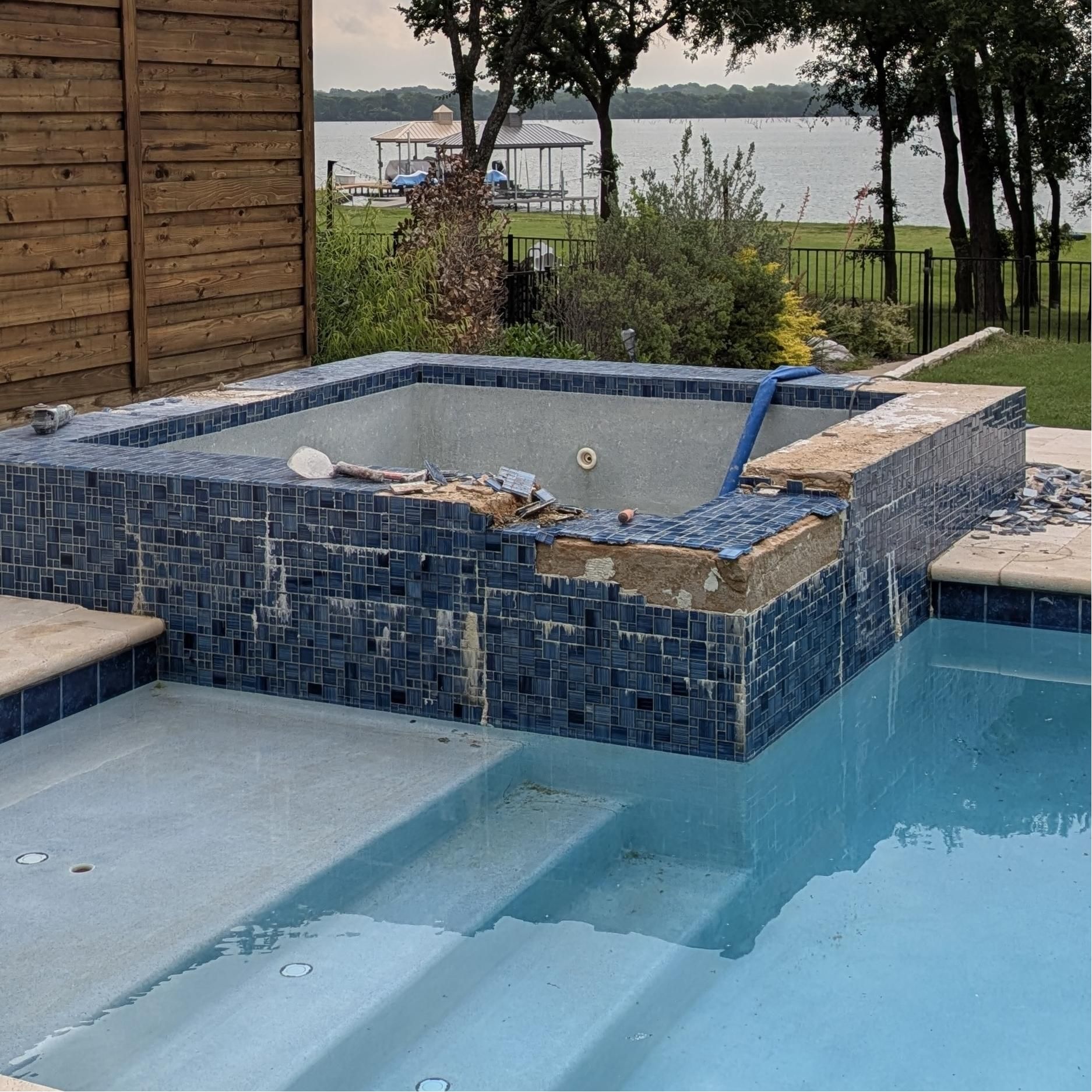 Hot tub and pool with blue tile. Lake and trees in the background. Construction in progress.