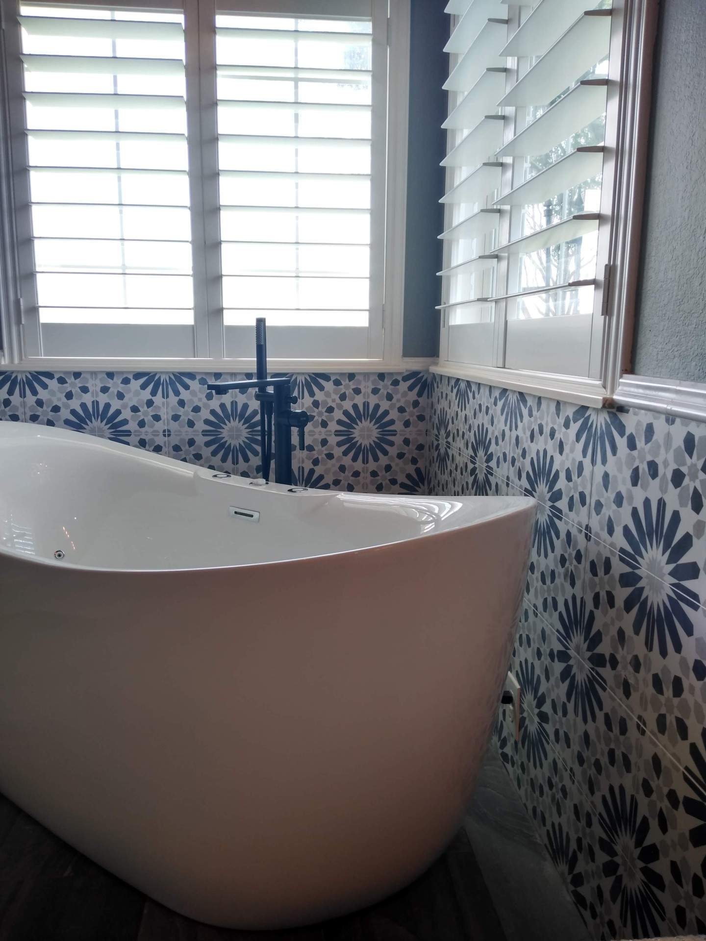 A bathtub in a bathroom with blue and white tiles and shutters.