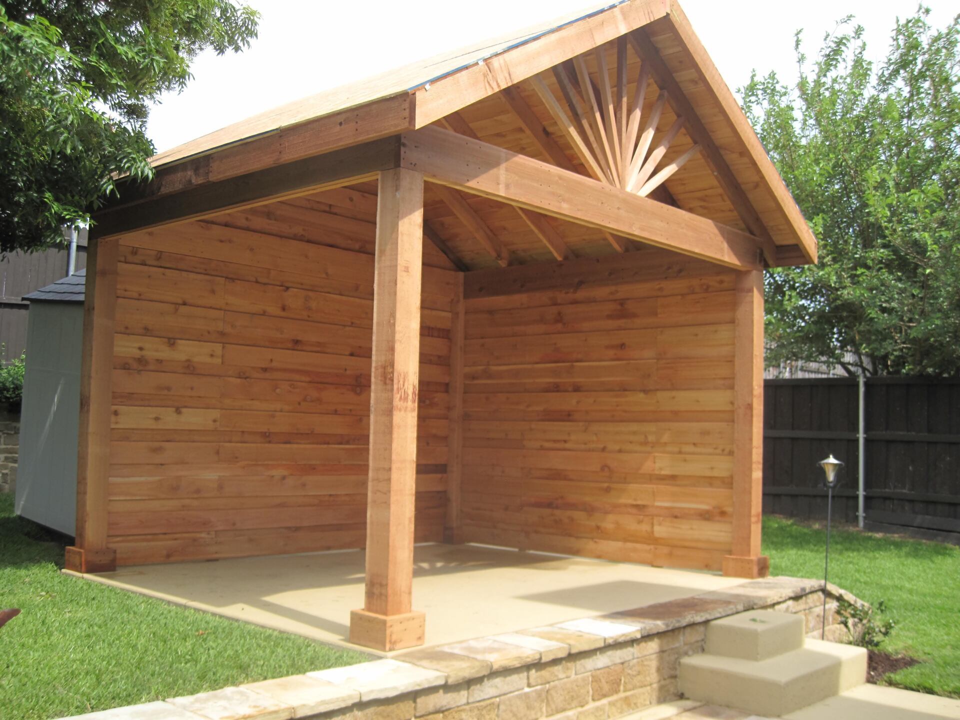 A wooden pavilion is sitting in the middle of a backyard.