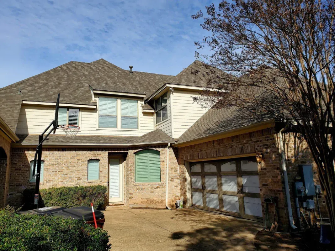 Brick house with brown roof, garage, and front door, blue sky in the background.
