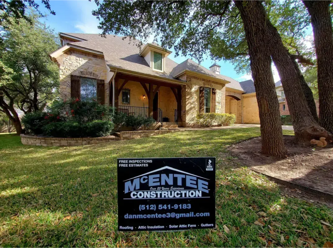 House with beige stone facade and brown trim. Sign for McEntee Construction in yard.