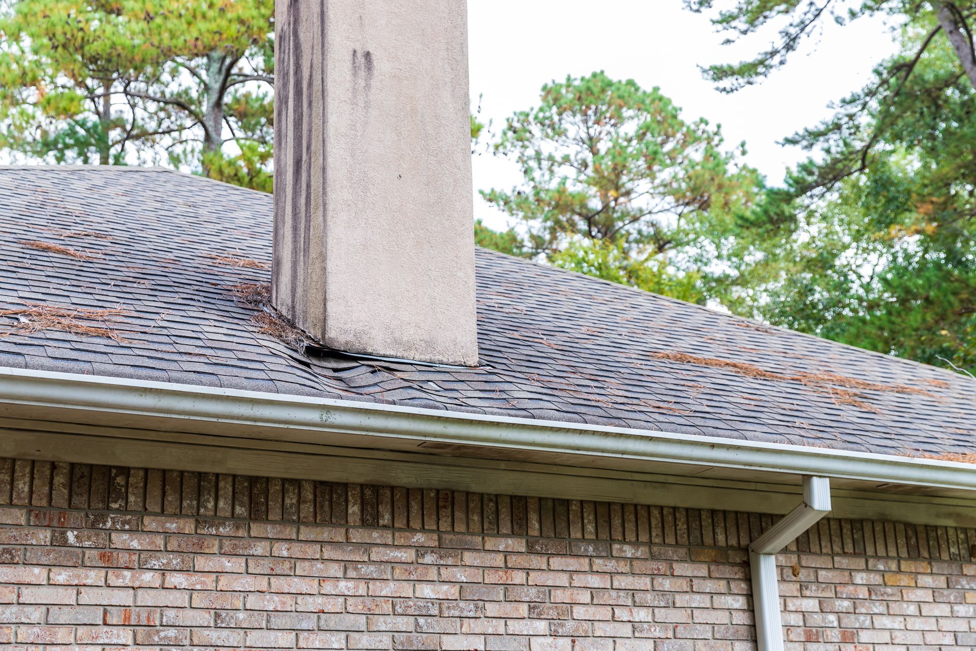 Roof with chimney, visible brick wall, and gutter. The roof has some debris.