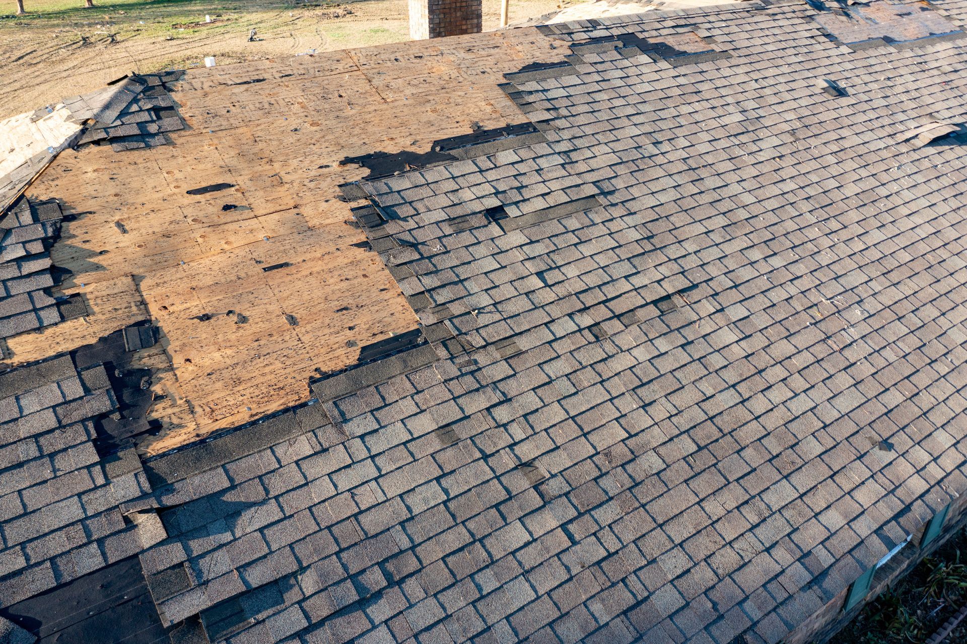 Damaged asphalt shingle roof, with missing shingles and exposed underlayment.