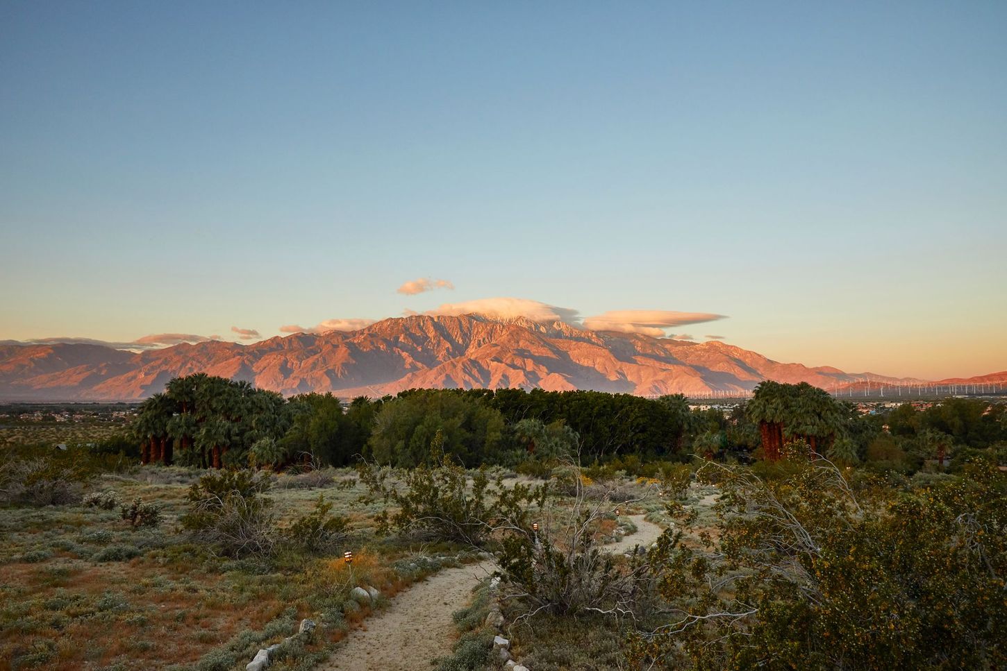 A dirt path in the desert with mountains in the background at sunset.