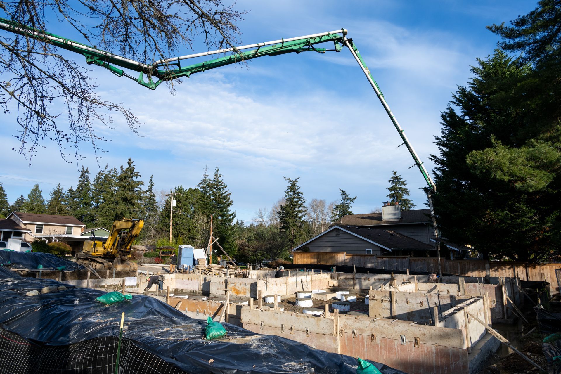 Concrete pump pouring at a construction site with foundation forms, equipment, and trees nearby