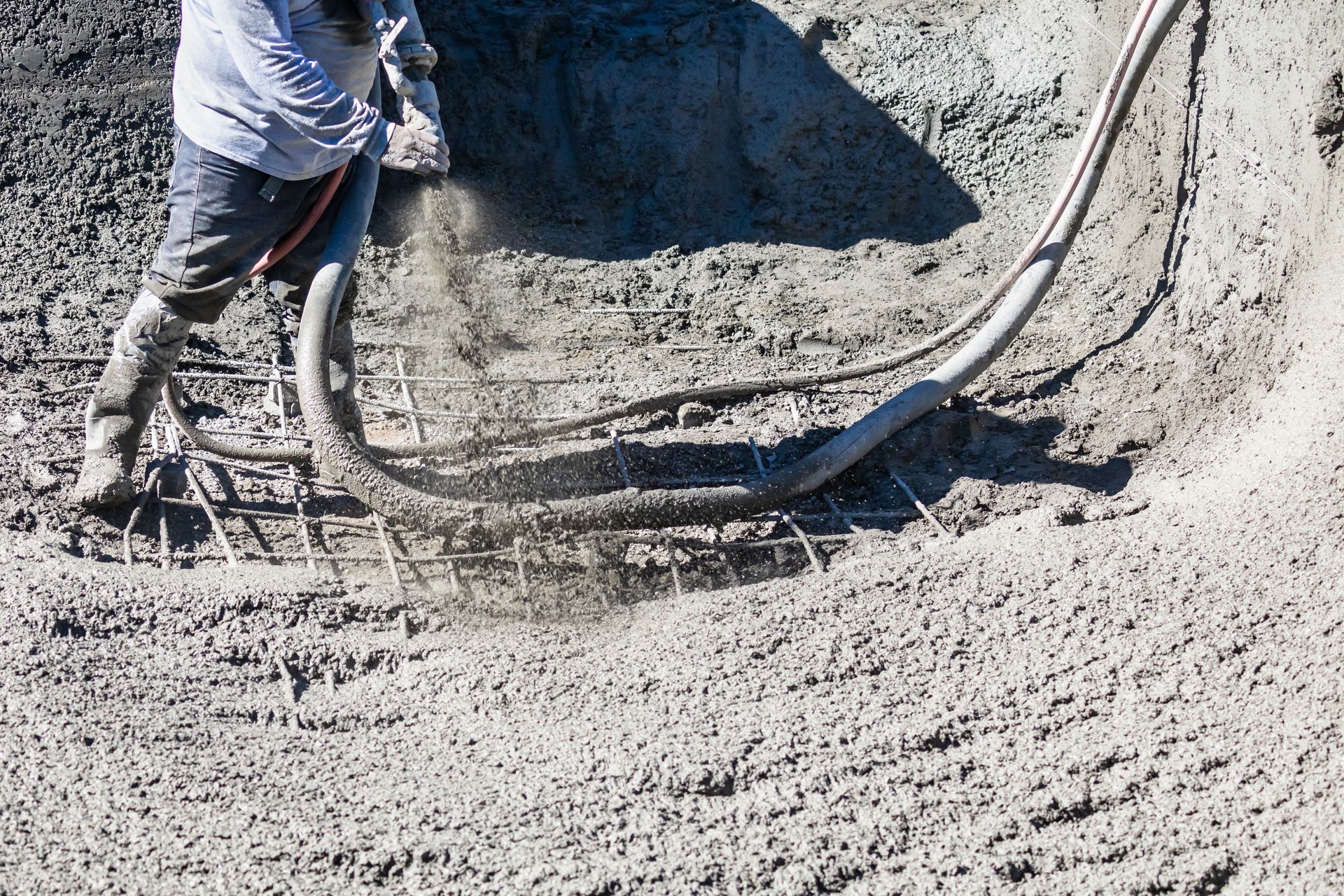 Worker spraying concrete into a curved excavation with hoses attached to a machine Worker spraying concrete into a curved excavation with hoses attached to a machine