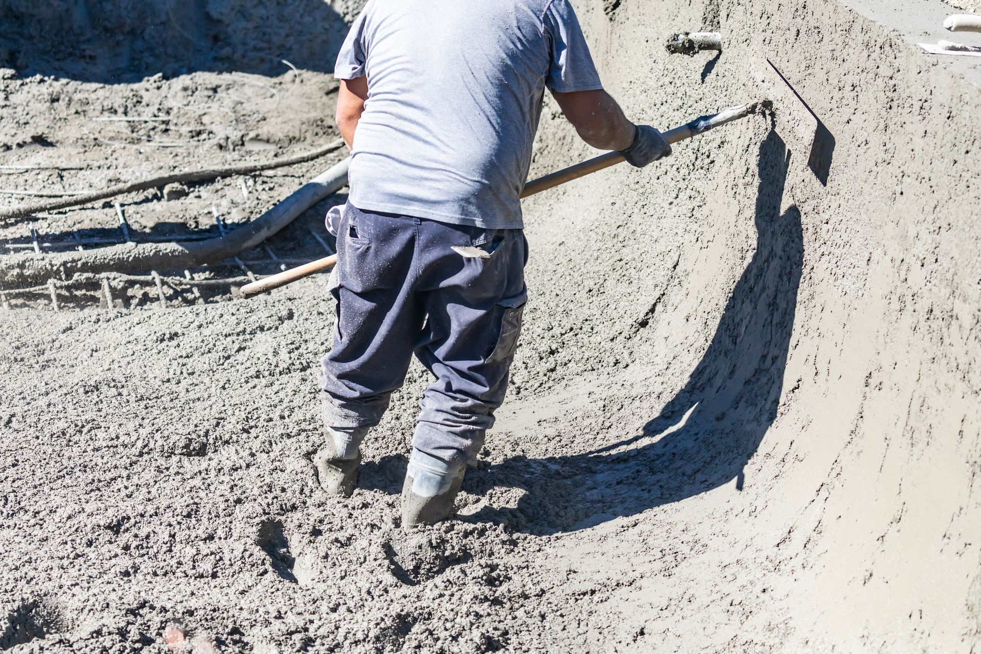Worker smoothing wet concrete with a tool at a construction site