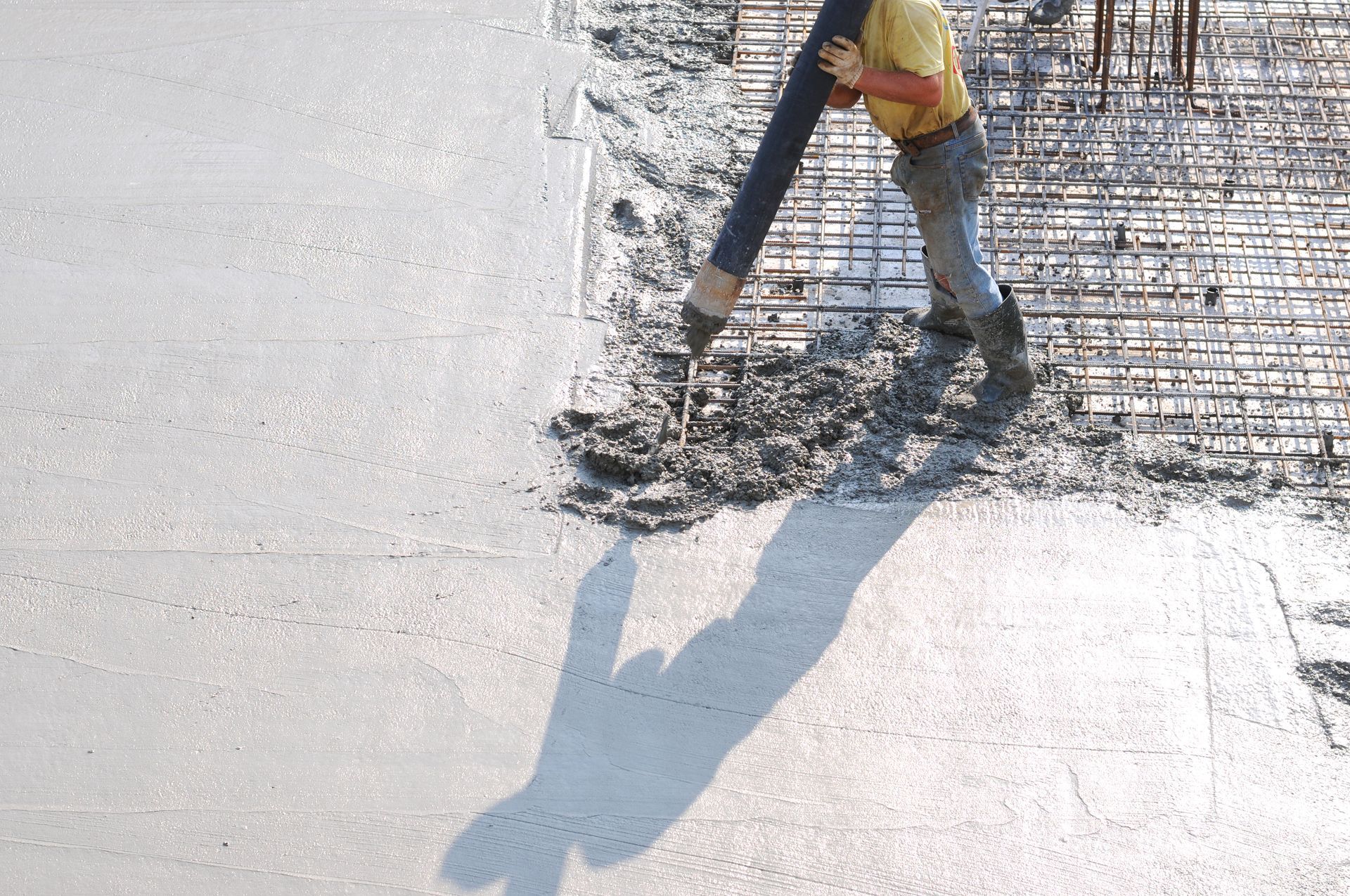 Worker using a hose to spray concrete on a construction site, casting a long shadow Worker using a hose to spray concrete on a construction site, casting a long shadow