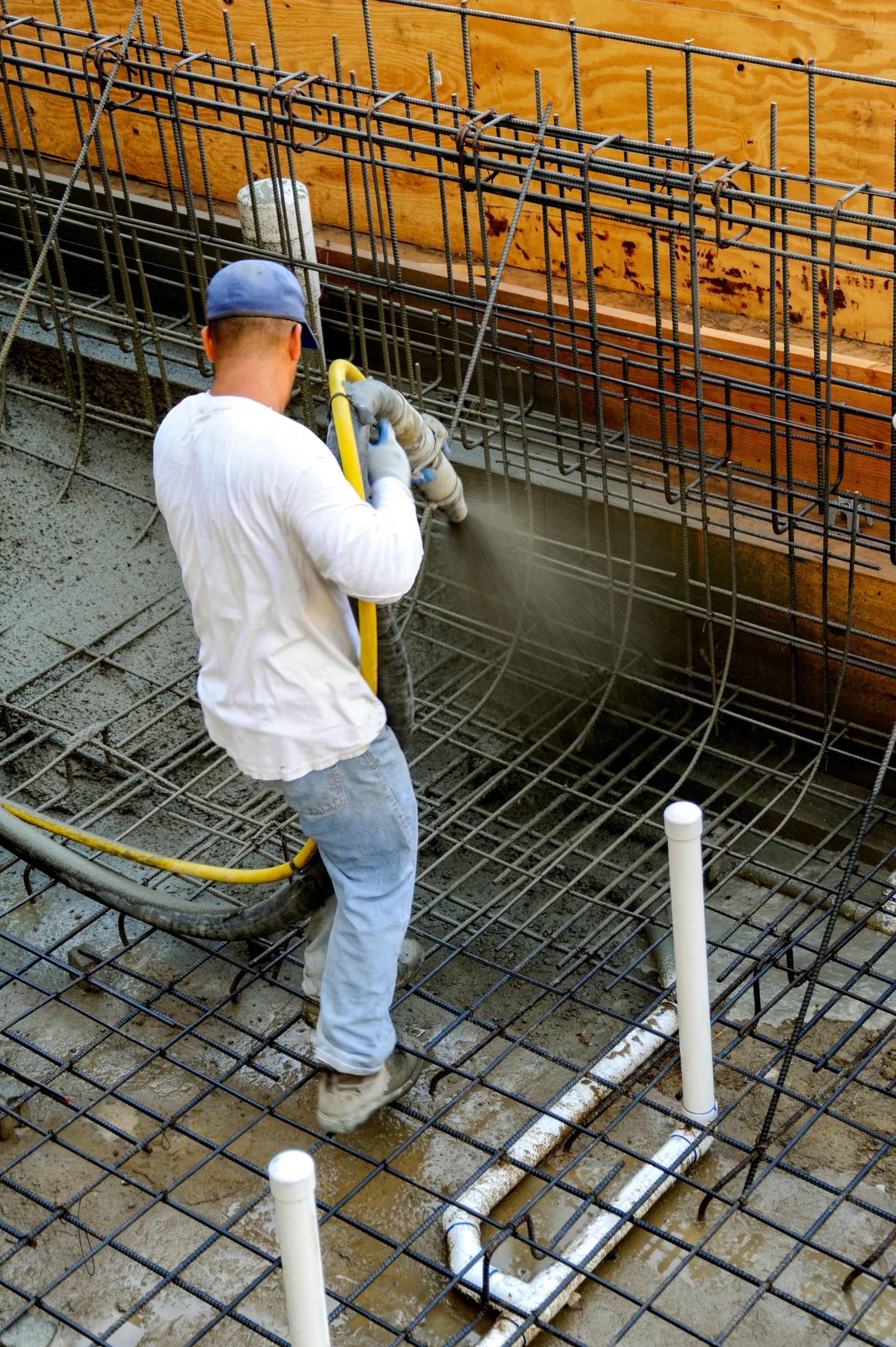 Worker spraying concrete onto rebar wall at a construction site Worker spraying concrete onto rebar wall at a construction site